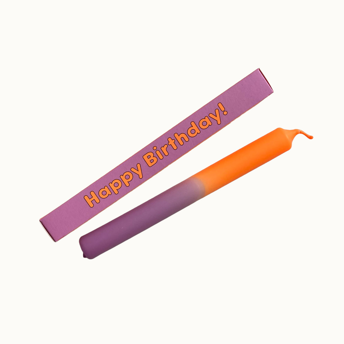 Eine zweifarbige Dip-Dye-Stabkerze in Orange und Flieder von Pink Stories, platziert neben der pinken Geschenkbox mit der Aufschrift „Happy Birthday!“