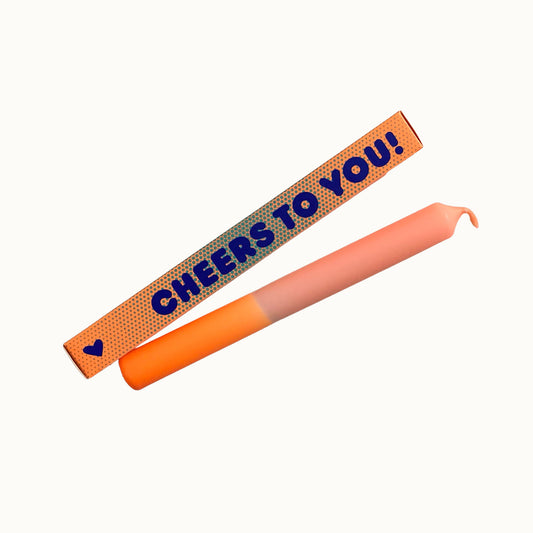 Eine sanft getauchte Stabkerze von Pink Stories in Pfirsich und Orange, abgebildet mit der orangen Pünktchen-Geschenkbox und der Aufschrift „CHEERS TO YOU!“