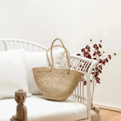 Großer Seegras-Shopper dekorativ auf einem weißen Rattan-Sessel platziert, umgeben von hellem Boho-Interieur.
