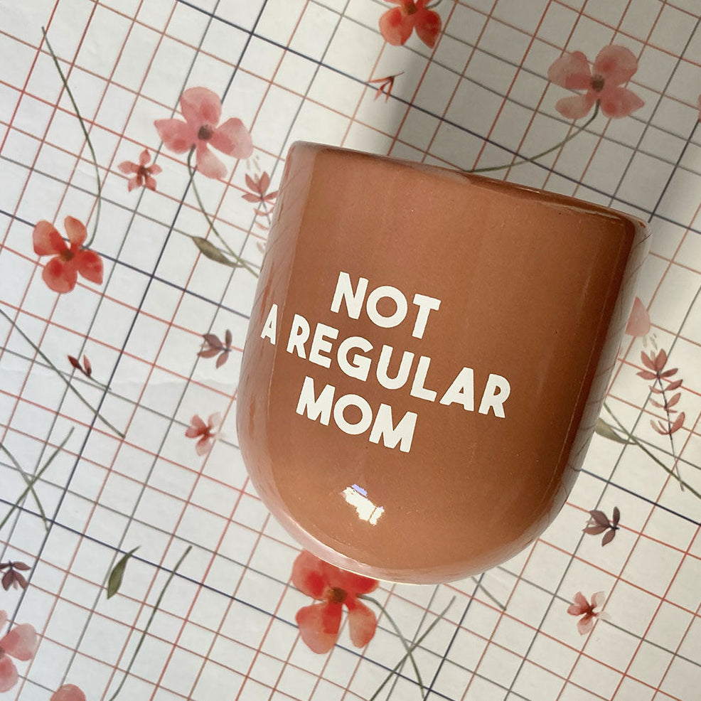 Braun-terracottafarbene Keramiktasse ohne Henkel von sisi house of style mit der weißen Aufschrift NOT A REGULAR MOM auf kariertem Blumenhintergrund.