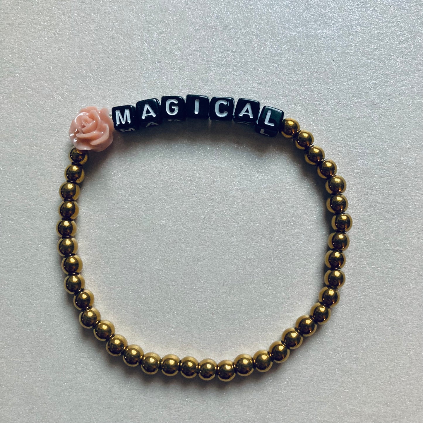 Minimalistisches Armband mit weißen Buchstaben-Perlen auf schwarzem Grund, Wortlaut MAGICAL, Länge 17,5 cm.