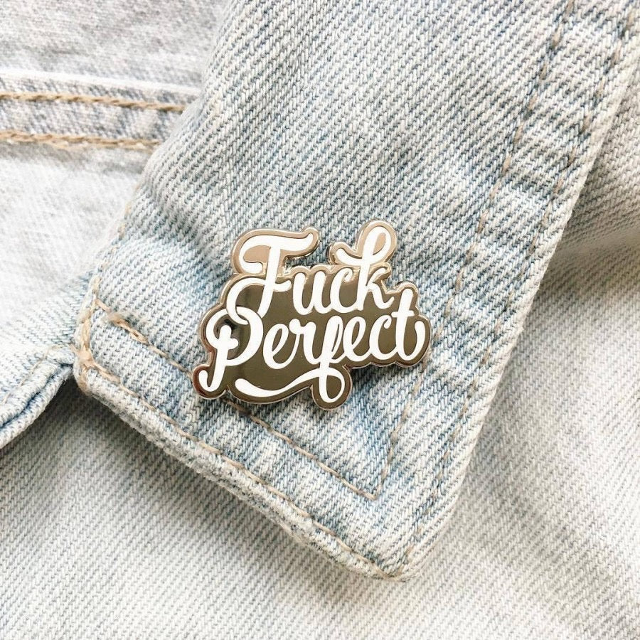 Anstecknadel mit dem Schriftzug 'Fuck Perfect' an einem hellen Jeansstoff befestigt