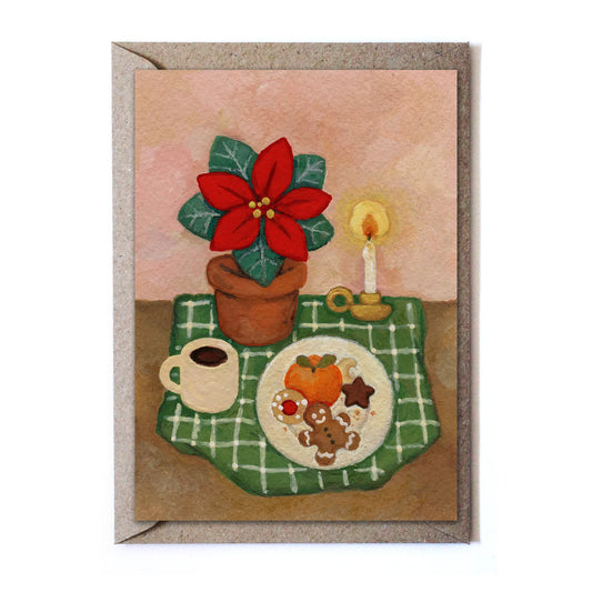 Studio Satsch Grußkarte mit einem herbstlich-winterlichen Stillleben: Ein roter Weihnachtsstern im Topf, eine brennende Kerze, eine Kaffeetasse und ein Teller mit Lebkuchenmann und Weihnachtskeksen auf einer grün karierten Decke.