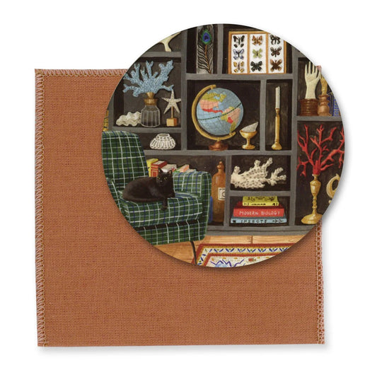 Runder Taschenspiegel mit einer detaillierten Illustration eines dunklen Regals voller Sammlerstücke wie einem Globus, Schmetterlingen und Korallen. Im Vordergrund schläft eine schwarze Katze in einem grün-blau karierten Sessel. Ein rostfarbene Schutzhülle liegt darunter.
