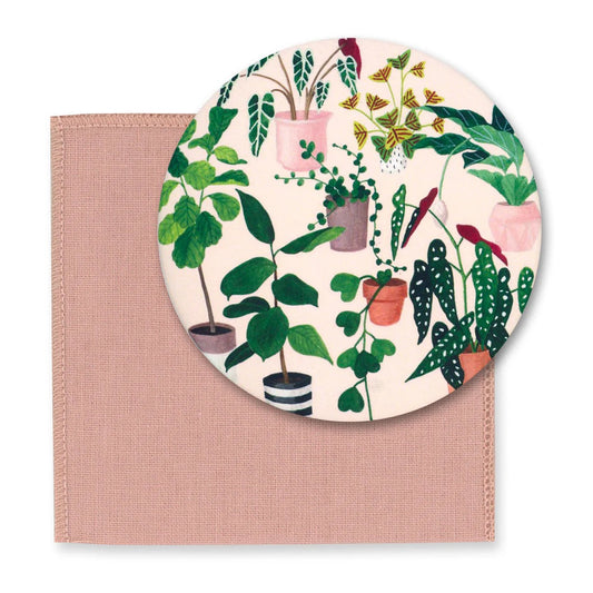 Runder Taschenspiegel mit einer Illustration verschiedener Zimmerpflanzen in bunten Töpfen (u.a. Ficus, Begonie und Hängepflanzen) auf beigem Hintergrund. Darunter liegt ein quadratisches, altrosa Schutztuch aus Mikrofaser.