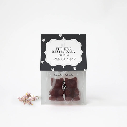 Zwei braune Bären aus Schokolade in transparenter Verpackung mit schwarzem Etikett, darauf steht 'FÜR DEN BESTEN PAPA TEEBÄRLI Hab dich lieb!'
