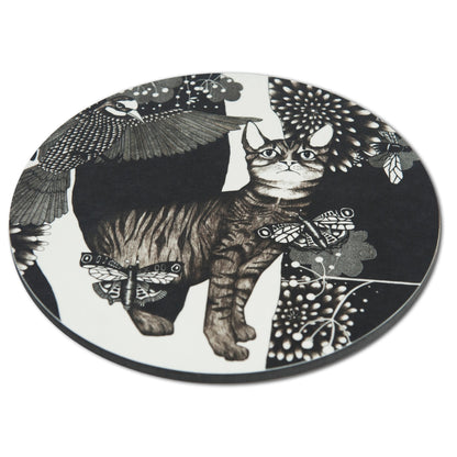 Schräge Seitenansicht des runden Nadja Wedin Topfuntersetzers zeigt die flache Form und die detailreiche Grafik mit Katze, Schmetterlingen und Vogel im schwarz-weißen Design.
