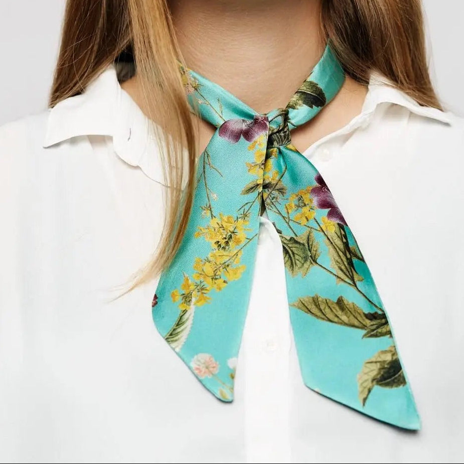 Türkisgrüner Twilly-Schal mit Botanik-Print, locker geknotet über einer weißen Hemdbluse.