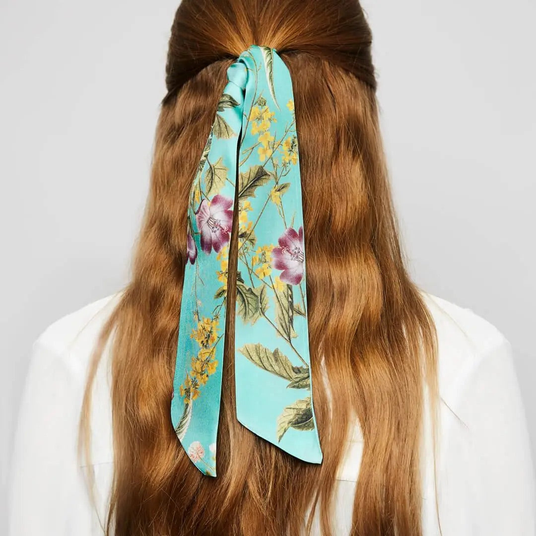 Lange braune Haare, die mit einem türkisfarbenen floralen Twilly-Band zusammengebunden sind.