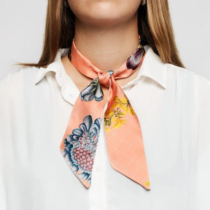 Nahaufnahme einer Frau, die einen rosa floralen Twilly-Schal mit einem kleinen Knoten zur weißen Bluse trägt.