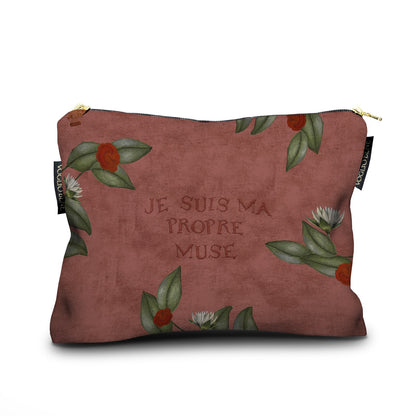 Eine Kosmetiktasche aus Stoff in einem warmen, erdigen Terrakotta-Ton. In der Mitte ist der französische Schriftzug „JE SUIS MA PROPRE MUSE“ eingeprägt. Der Rand ist dezent mit grünen Blättern sowie kleinen roten und weißen Blüten verziert. Die Tasche schließt mit einem goldenen Reißverschluss und zeigt an den Seiten schwarze Markenetiketten mit der Aufschrift „VOGLIO BENE“.